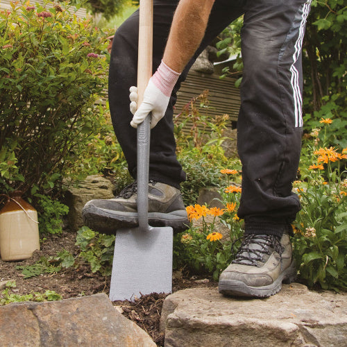 Persoon gebruikt een spade met opstapje in de tuin tussen bloemen en stenen.